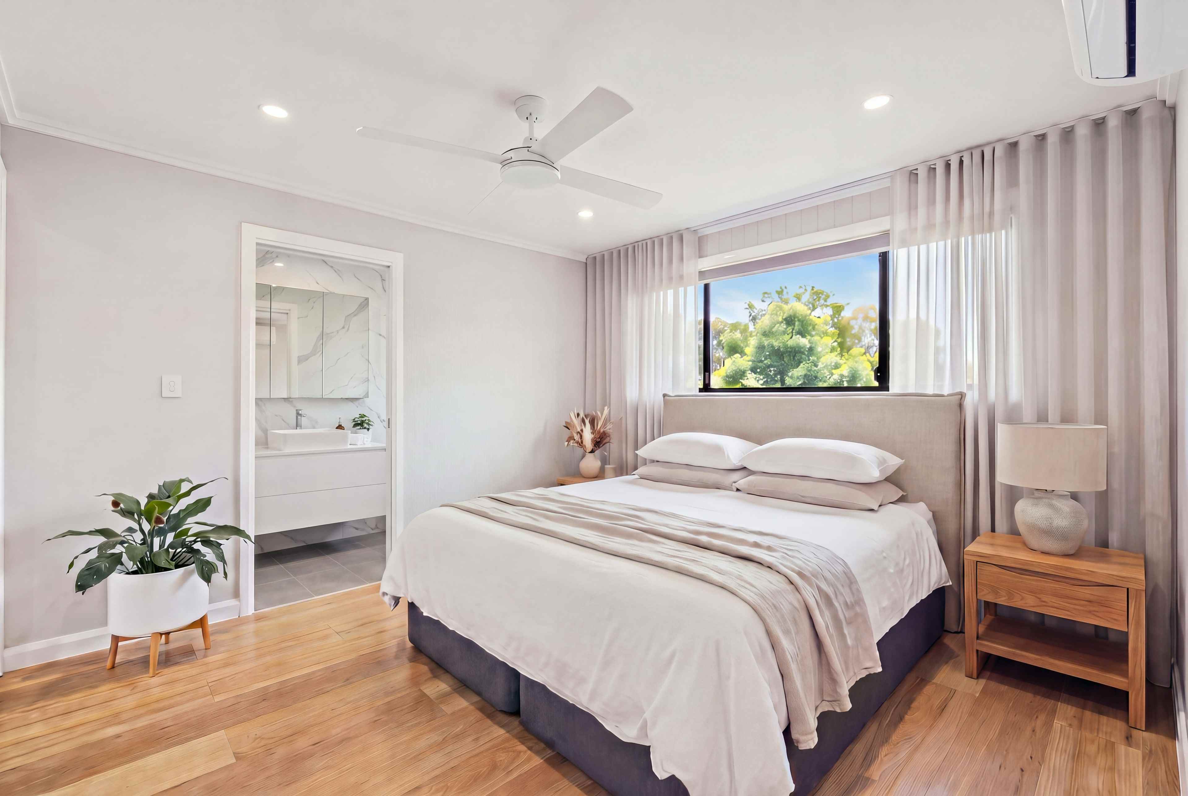 Main bedroom with a linen bedhead, oak bedside tables and sheer curtains