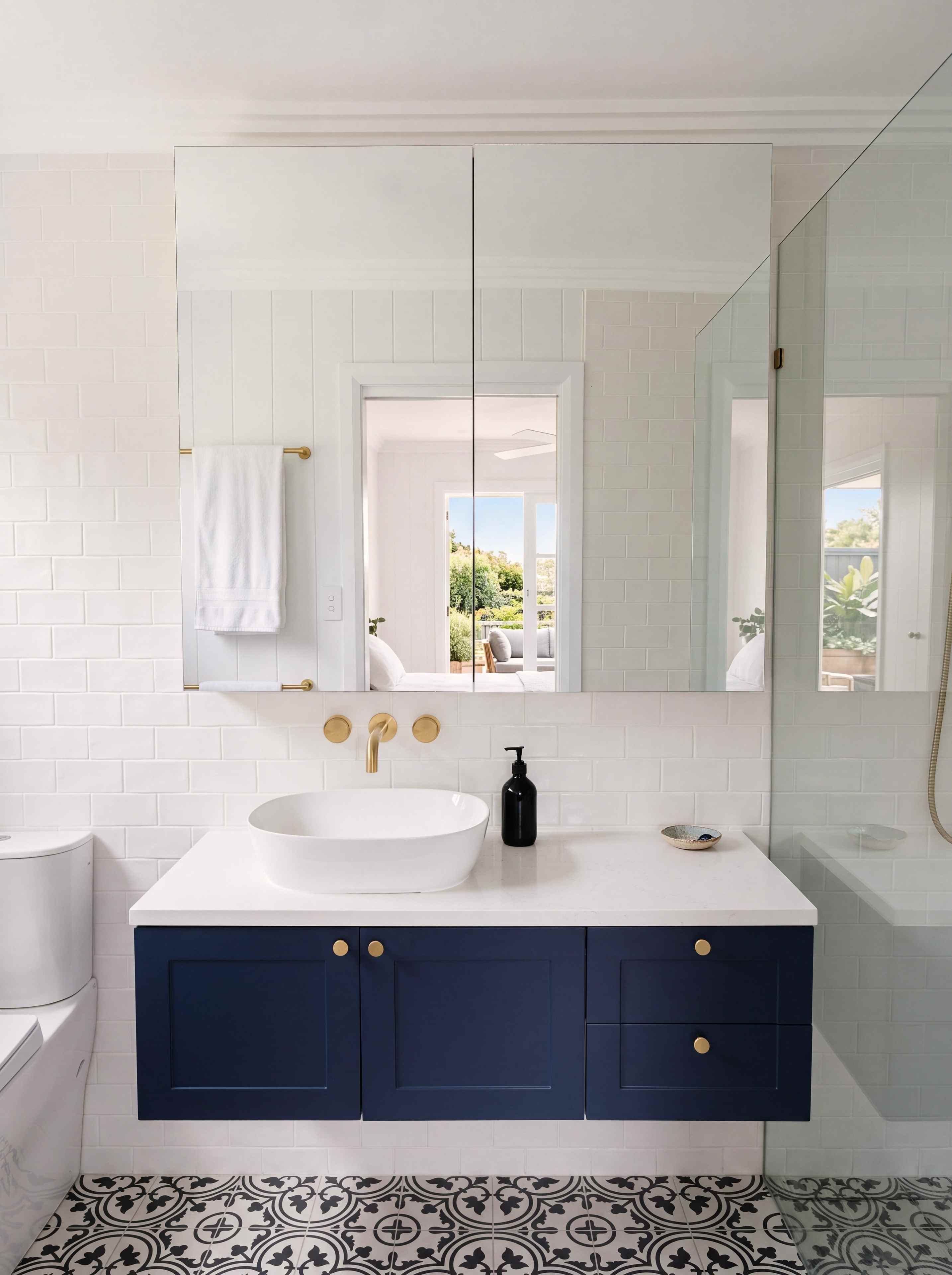 Navy shaker vanity with brass knobs over black and white patterned floor tiles in the ensuite