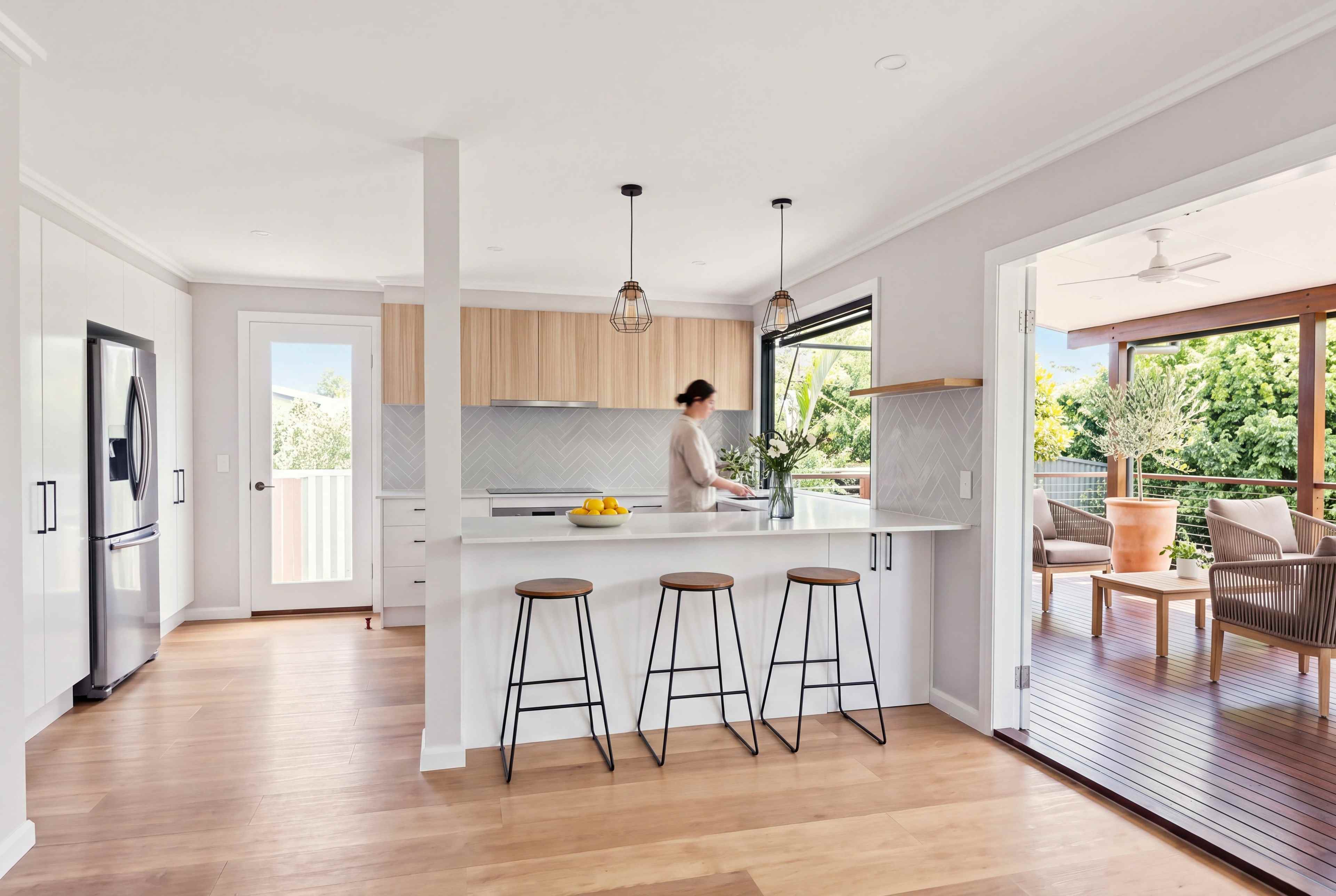 Open-plan kitchen with an island and three stools, opening onto the covered deck in soft daylight