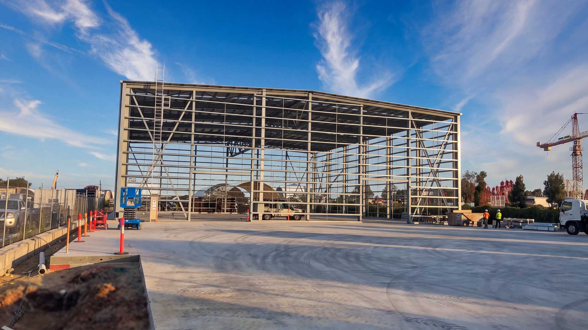 A large steel-framed industrial building rising over a new concrete hardstand in golden light