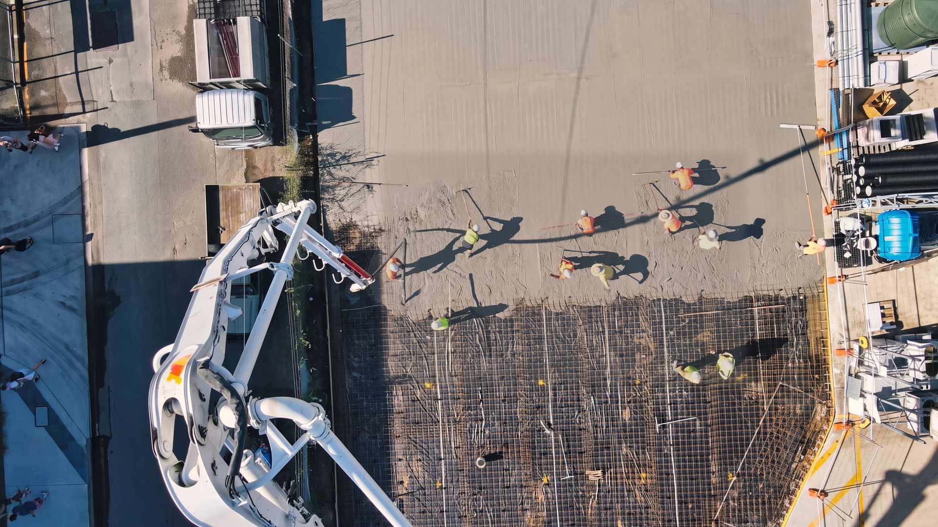 Seen from above, a concrete pump boom reaches over a slab while the crew screeds fresh concrete over steel mesh