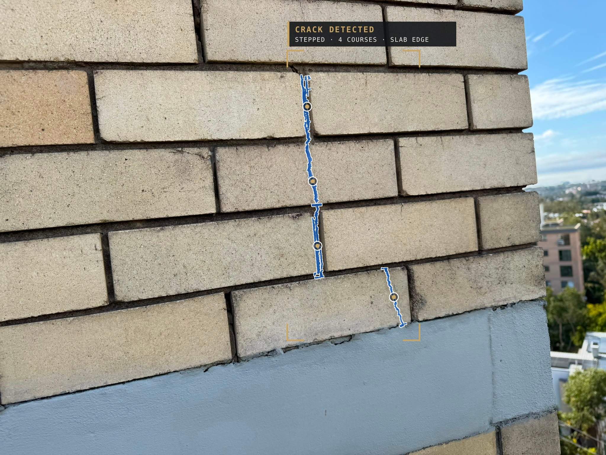 The same brickwork with the crack detected: a blue segmentation mask along a stepped crack through four courses and a split brick above the slab edge, inside a brass detection frame labelled Crack detected